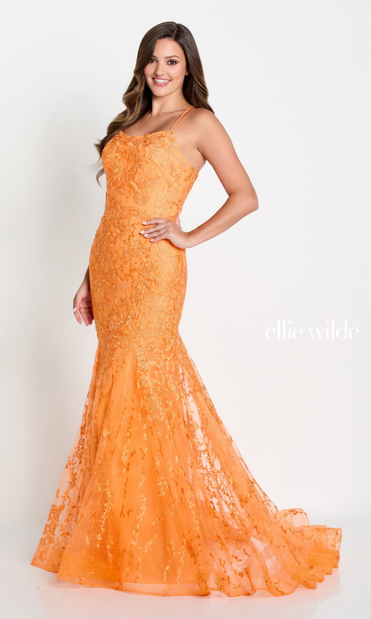 A woman models the Long Lace Mermaid Prom Dress with Strappy Back—fitted, floor-length, orange lace with thin straps and an open back—posing against a white background. “Ellie Wilde” appears beside her.